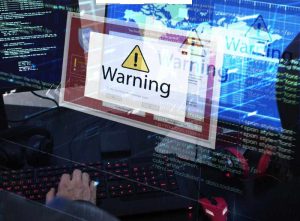 A computer is being hacked with a warning pop-up sign.